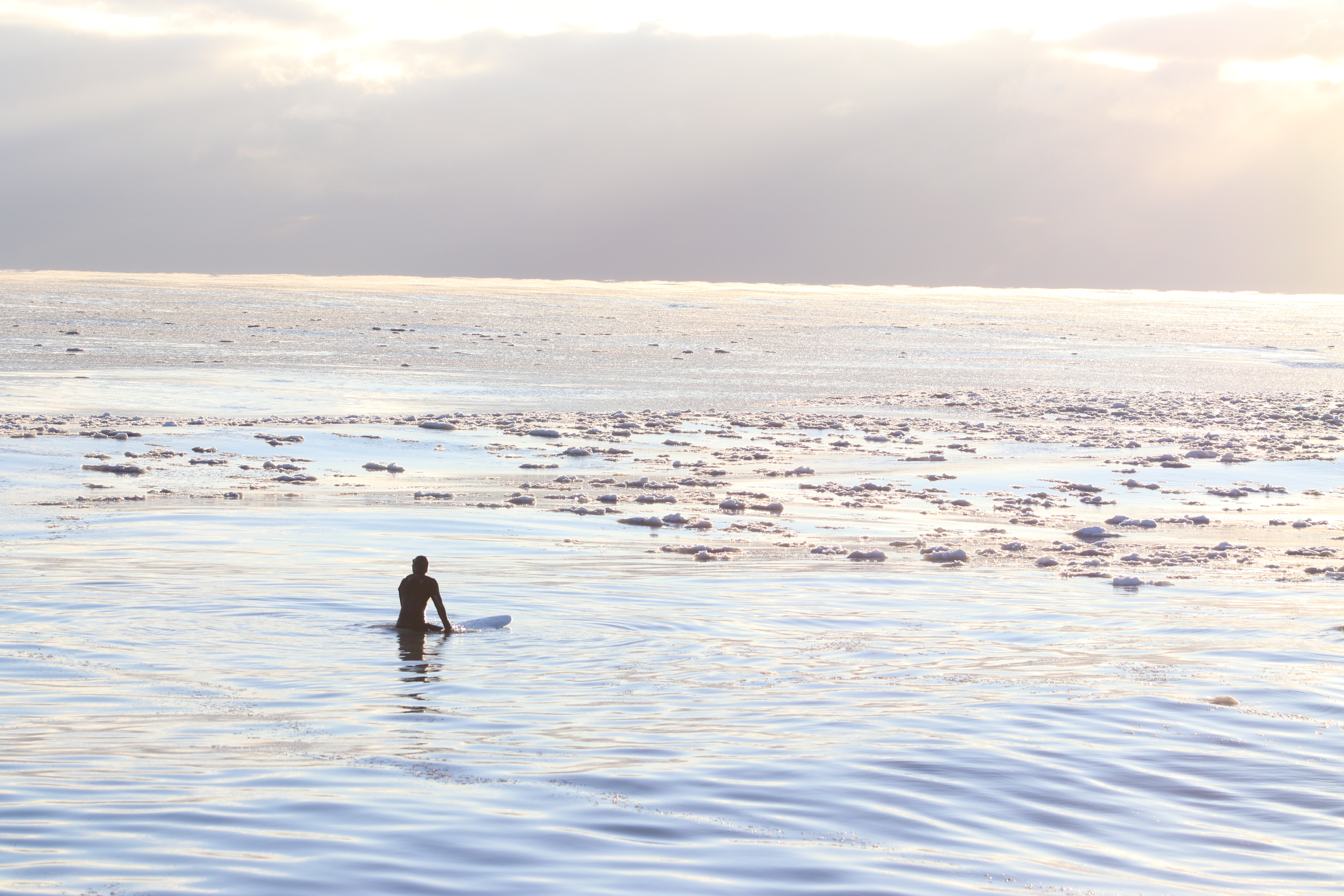 surfer in wetsuit staring at the horizon surrounded by ice in Lake Michigan, Chicago